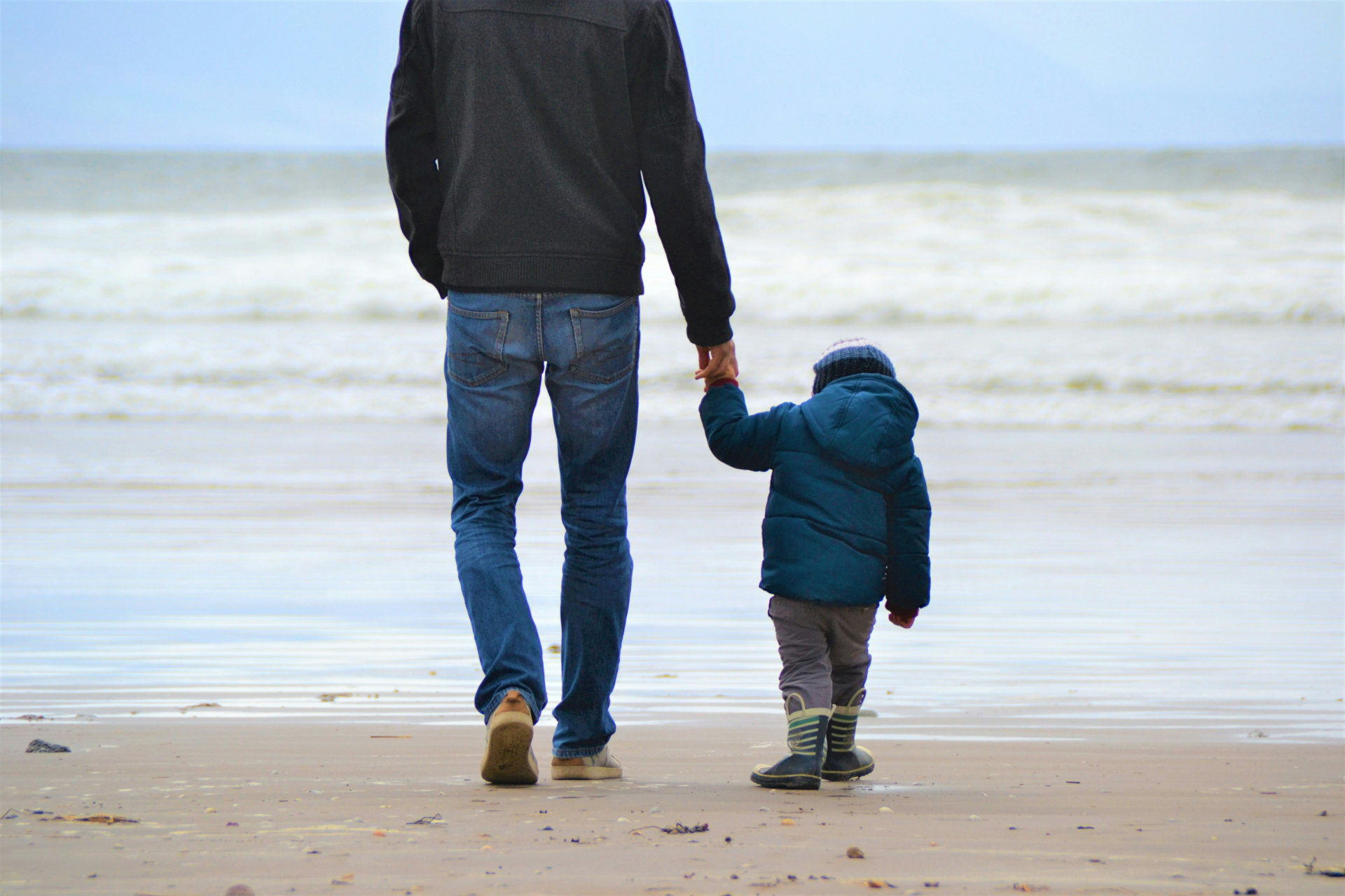 Un homme tient un enfant par la main sur une plage