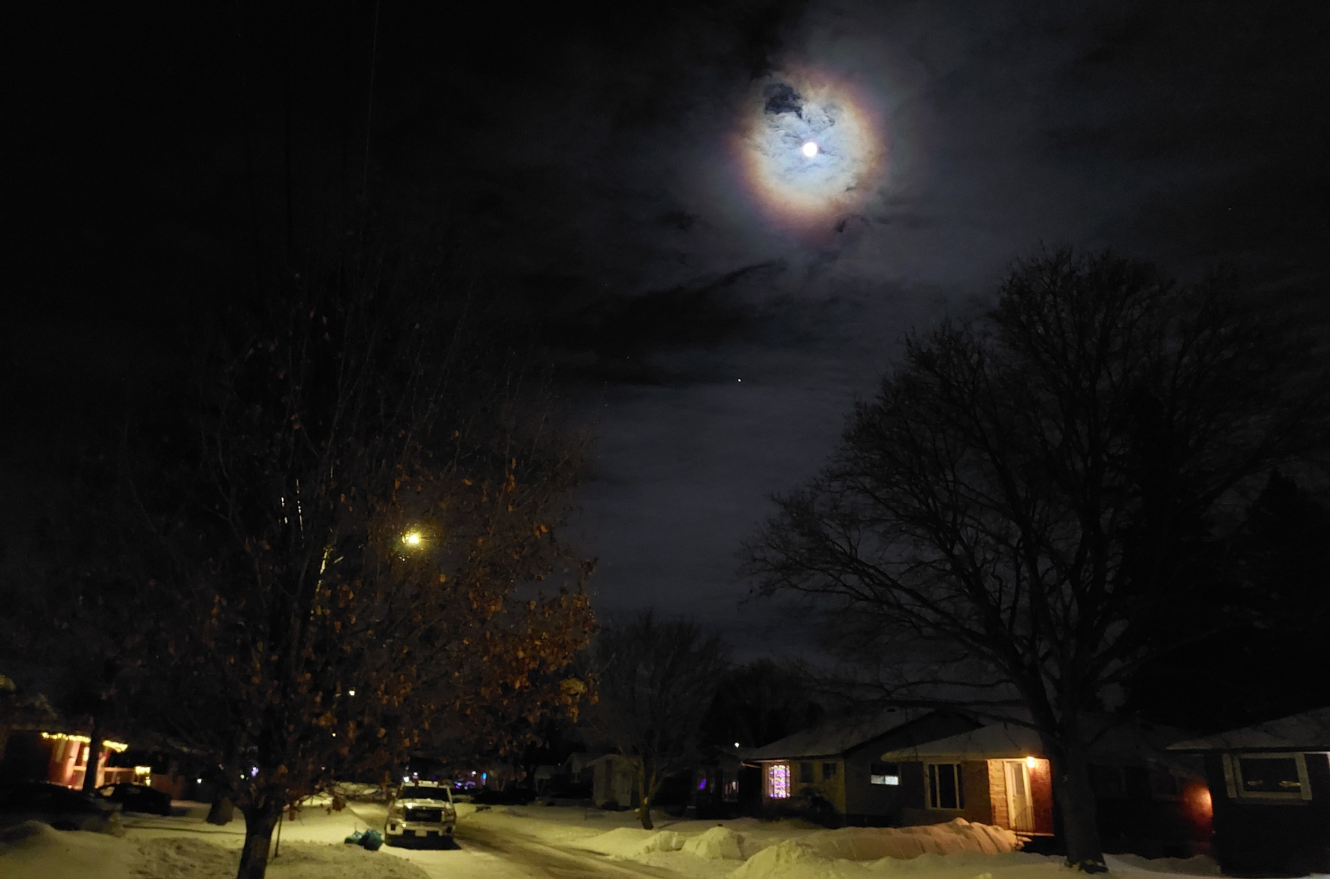 Rue avec la lune entourée d'un halo arc-en-ciel dans la nuit