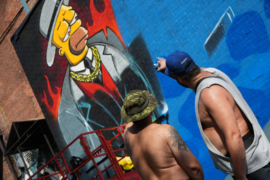 Deux grapheurs au pied d'une facade avec un graffiti de Homer Simpson